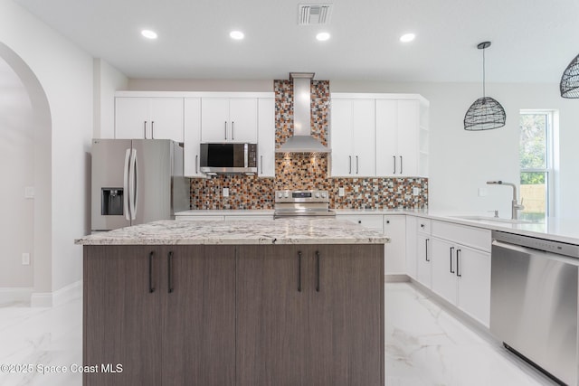 kitchen featuring wall chimney range hood, sink, stainless steel appliances, white cabinets, and decorative light fixtures