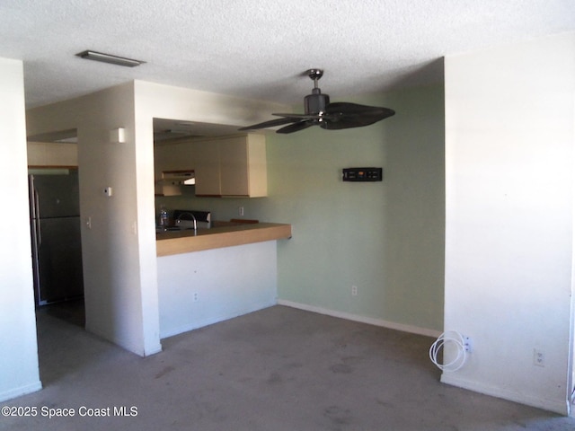 kitchen with black refrigerator, sink, ceiling fan, kitchen peninsula, and a textured ceiling