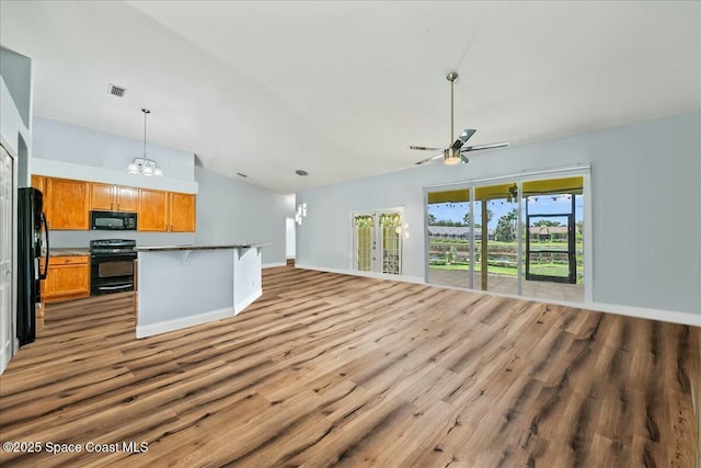 kitchen with vaulted ceiling, a breakfast bar area, hanging light fixtures, black appliances, and light wood-type flooring