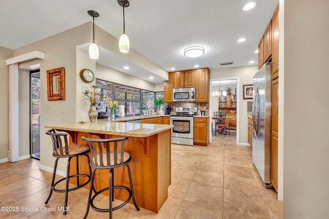 kitchen featuring decorative light fixtures, a breakfast bar area, backsplash, kitchen peninsula, and stainless steel appliances