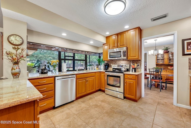 kitchen with pendant lighting, appliances with stainless steel finishes, light stone countertops, decorative backsplash, and kitchen peninsula