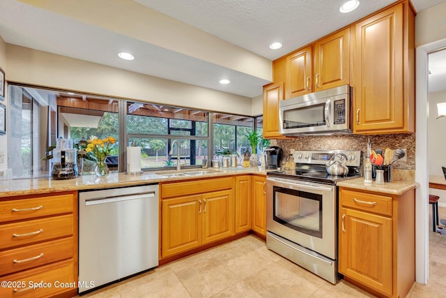 kitchen with sink, appliances with stainless steel finishes, backsplash, light stone countertops, and a textured ceiling