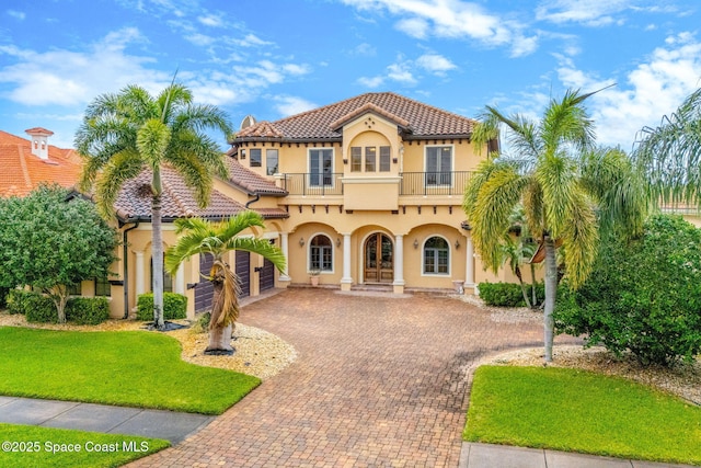 mediterranean / spanish home with decorative driveway, a tile roof, a balcony, and stucco siding