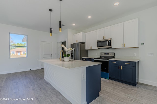 kitchen with white cabinetry, hanging light fixtures, light hardwood / wood-style flooring, appliances with stainless steel finishes, and an island with sink