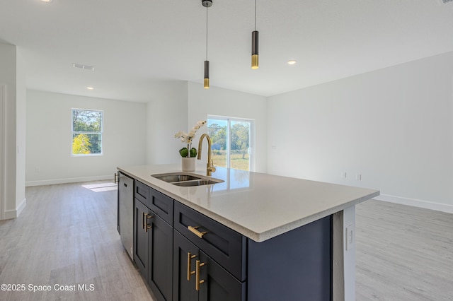 kitchen with sink, decorative light fixtures, light hardwood / wood-style floors, and a center island with sink