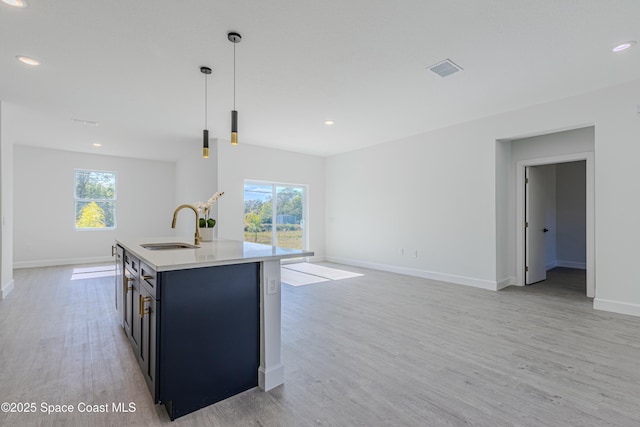 kitchen with hanging light fixtures, light wood-type flooring, sink, and a center island with sink