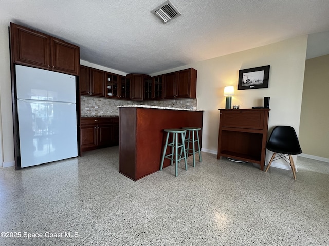 kitchen with decorative backsplash, kitchen peninsula, a textured ceiling, and white fridge