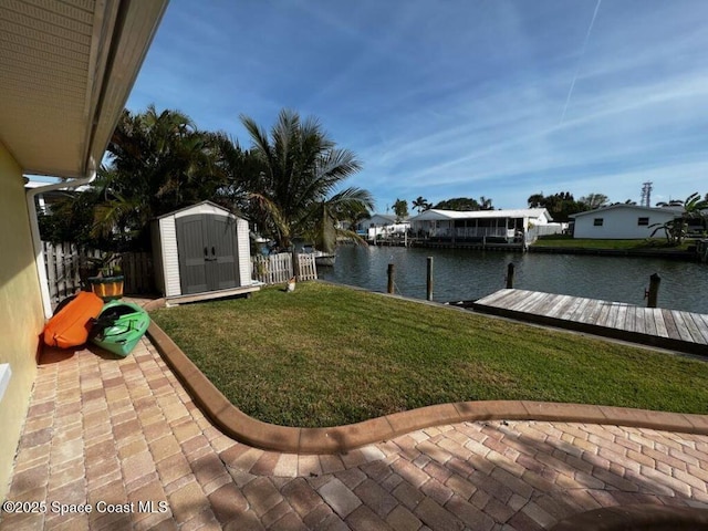 view of yard with a water view, a dock, a shed, and a patio area