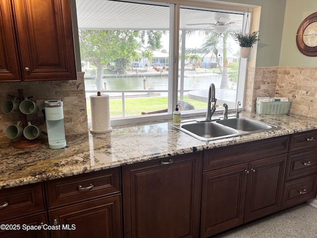 kitchen featuring sink, decorative backsplash, light stone countertops, and a water view