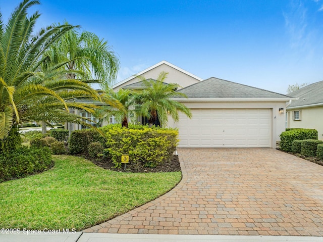 view of front facade with decorative driveway, stucco siding, a shingled roof, a front yard, and a garage