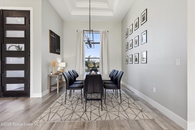 dining room with a high ceiling, ornamental molding, light hardwood / wood-style floors, a raised ceiling, and an inviting chandelier