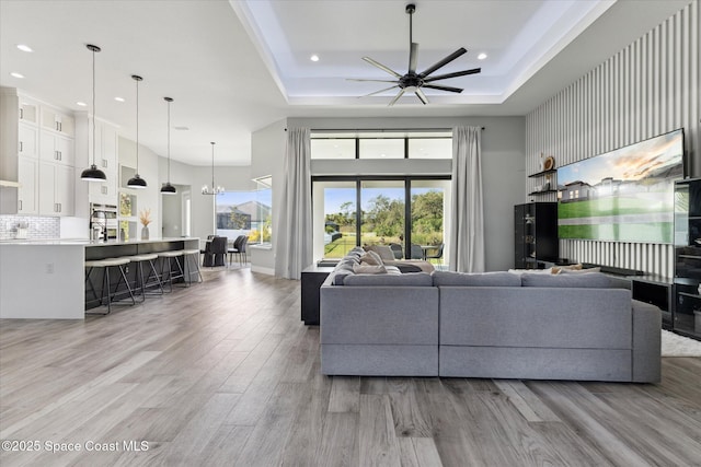 living room with a towering ceiling, a raised ceiling, ceiling fan with notable chandelier, and light hardwood / wood-style flooring