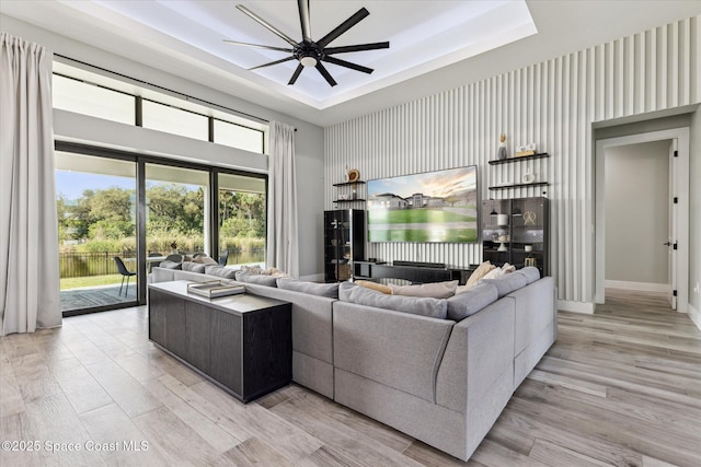 living room featuring a water view, ceiling fan, a raised ceiling, and light hardwood / wood-style flooring