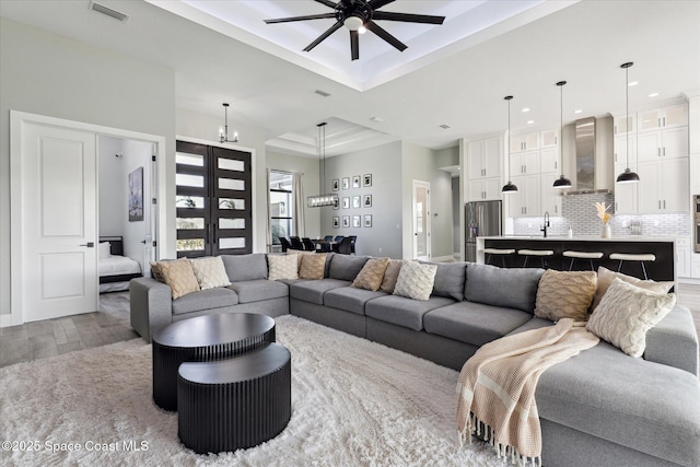 living room featuring sink, ceiling fan with notable chandelier, light hardwood / wood-style flooring, and a raised ceiling