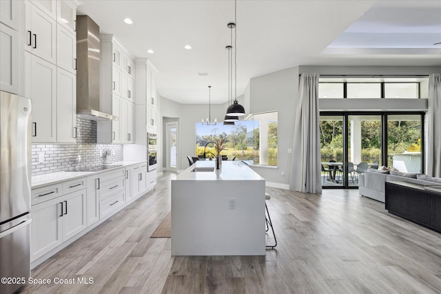 kitchen with appliances with stainless steel finishes, sink, white cabinets, a kitchen island with sink, and wall chimney range hood