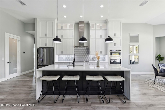 kitchen with stainless steel appliances, a kitchen island with sink, sink, and wall chimney range hood