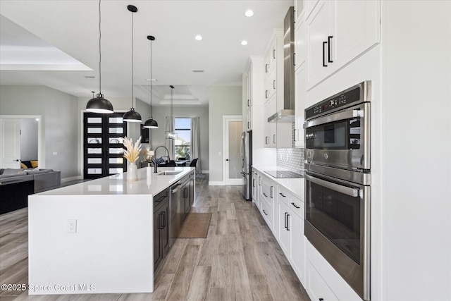 kitchen with pendant lighting, sink, stainless steel appliances, white cabinets, and a center island with sink