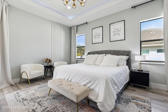 bedroom with a raised ceiling, hardwood / wood-style floors, and a notable chandelier