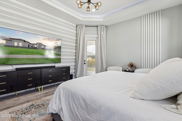 bedroom with a tray ceiling, a chandelier, light hardwood / wood-style floors, and access to outside