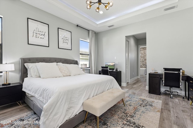 bedroom with a notable chandelier, light hardwood / wood-style flooring, and a raised ceiling