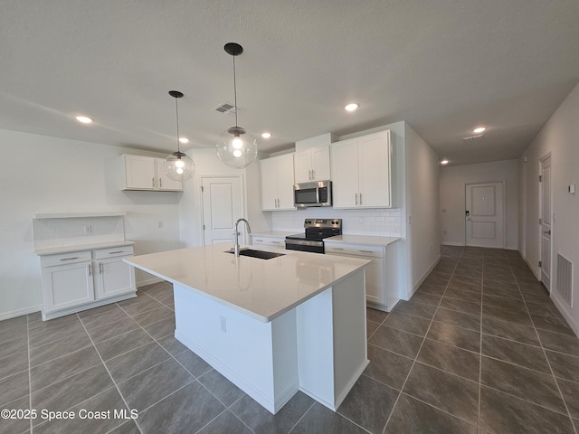 kitchen with sink, appliances with stainless steel finishes, an island with sink, dark tile patterned floors, and white cabinets