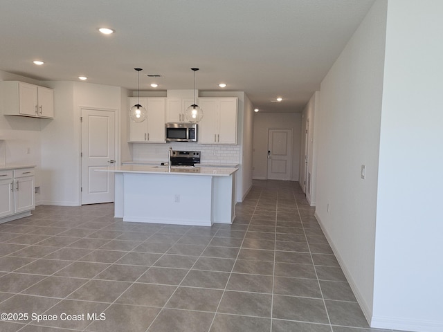 kitchen with appliances with stainless steel finishes, tasteful backsplash, white cabinetry, an island with sink, and hanging light fixtures