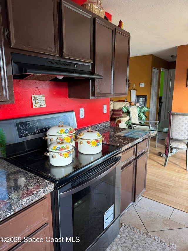 kitchen featuring dark brown cabinetry, black electric range oven, light tile patterned floors, and dark stone counters