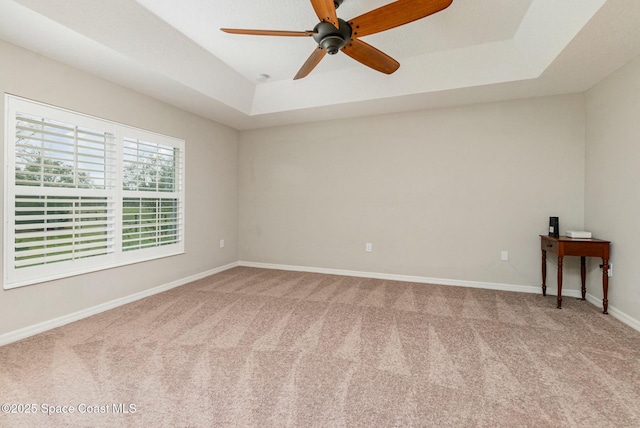 carpeted empty room featuring ceiling fan and a raised ceiling