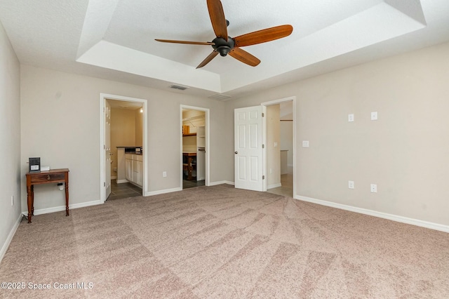 unfurnished bedroom featuring carpet, connected bathroom, a raised ceiling, a walk in closet, and a closet