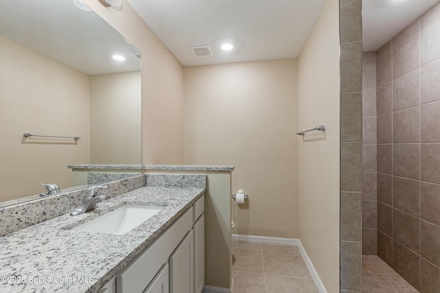 bathroom featuring vanity, tile patterned flooring, a textured ceiling, and a tile shower