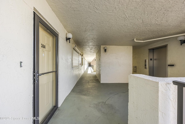 hall with elevator, concrete flooring, and a textured ceiling