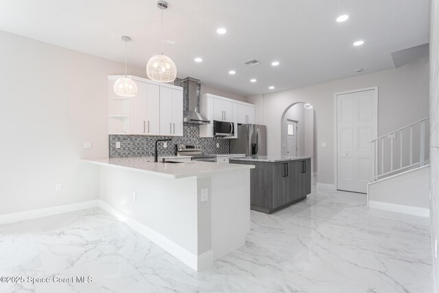 kitchen with wall chimney exhaust hood, hanging light fixtures, a kitchen island, stainless steel appliances, and white cabinets