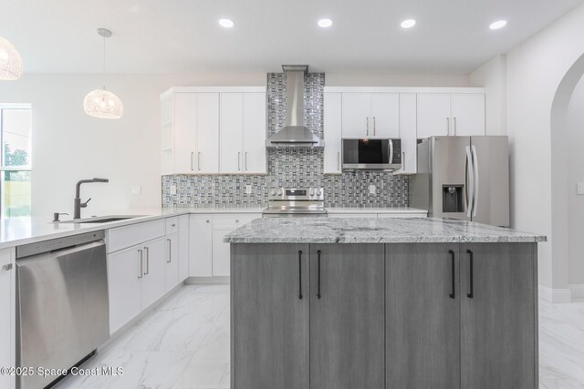 kitchen with sink, decorative light fixtures, wall chimney range hood, stainless steel appliances, and white cabinets