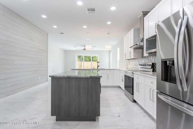 kitchen with appliances with stainless steel finishes, decorative light fixtures, wood walls, white cabinets, and kitchen peninsula