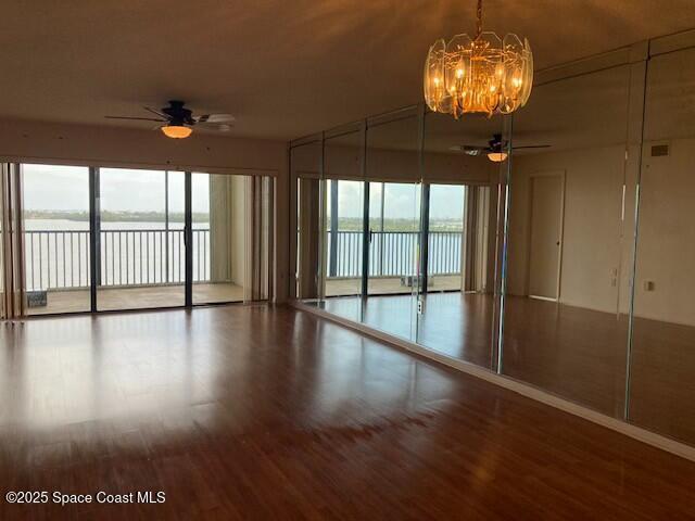 spare room with hardwood / wood-style floors, ceiling fan with notable chandelier, and a water view