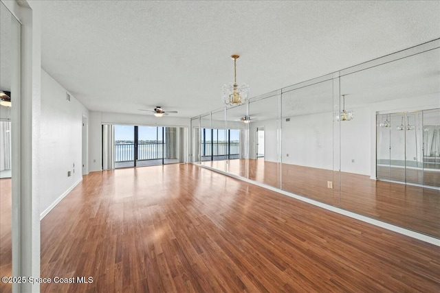 unfurnished living room with ceiling fan with notable chandelier, hardwood / wood-style floors, and a textured ceiling