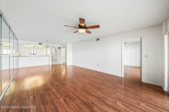 unfurnished living room featuring ceiling fan with notable chandelier, hardwood / wood-style floors, and a textured ceiling