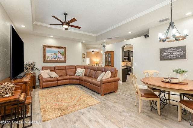 living room with ornamental molding, ceiling fan with notable chandelier, light hardwood / wood-style flooring, and a tray ceiling