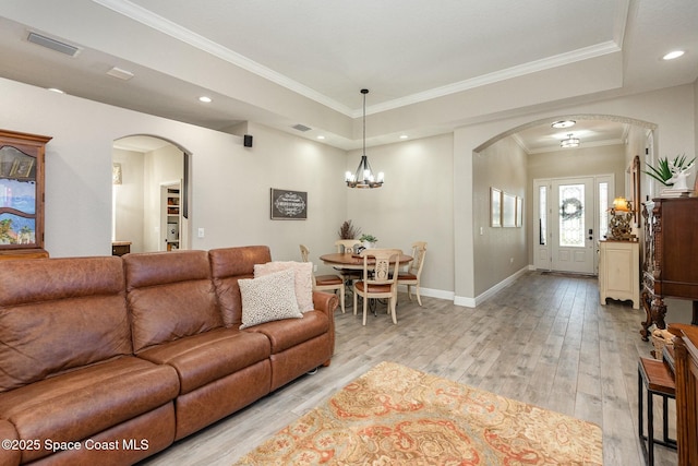 living room featuring crown molding, a notable chandelier, a raised ceiling, and light wood-type flooring