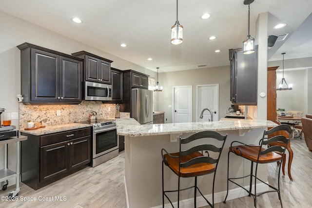 kitchen featuring stainless steel appliances, decorative light fixtures, light stone countertops, and decorative backsplash