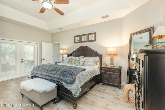 bedroom with access to outside, ceiling fan, light hardwood / wood-style floors, a raised ceiling, and french doors