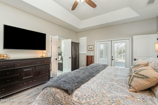 bedroom with light wood-type flooring, access to outside, a tray ceiling, ensuite bath, and french doors