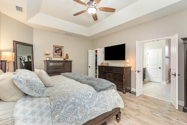 bedroom with ceiling fan, a tray ceiling, and light hardwood / wood-style floors