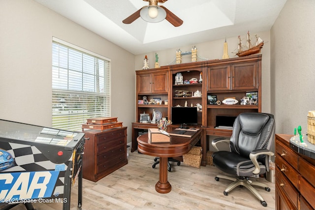 home office with a tray ceiling, light hardwood / wood-style flooring, and ceiling fan