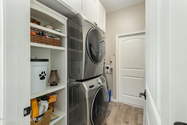 laundry room with stacked washer / dryer, cabinets, and light hardwood / wood-style floors