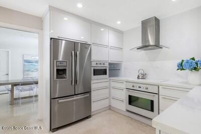 kitchen featuring white cabinetry, stainless steel fridge, wall chimney exhaust hood, and white oven