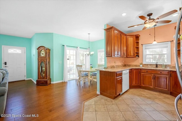 kitchen featuring sink, white dishwasher, light hardwood / wood-style floors, decorative light fixtures, and kitchen peninsula