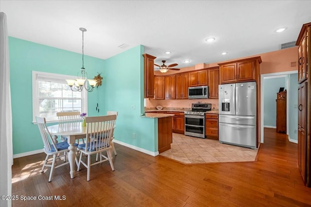 kitchen with light hardwood / wood-style flooring, appliances with stainless steel finishes, hanging light fixtures, light stone countertops, and ceiling fan with notable chandelier