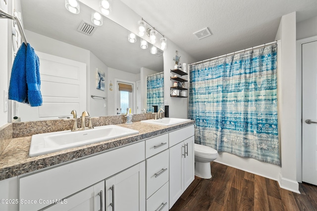 full bathroom featuring shower / bathtub combination with curtain, vanity, wood-type flooring, a textured ceiling, and toilet