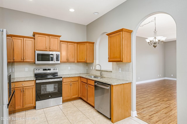 kitchen with sink, backsplash, stainless steel appliances, and light stone countertops